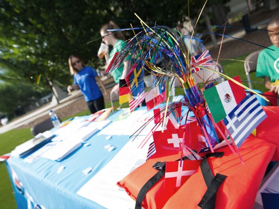 On the ground there is a table with flags of different countries. Two girls are standing near by the table and celebrating Welcoming Week.